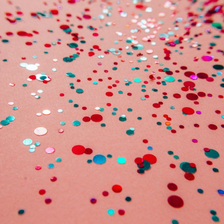 Bunte Glitzerpartikel auf einem rosa Hintergrund verstreut.