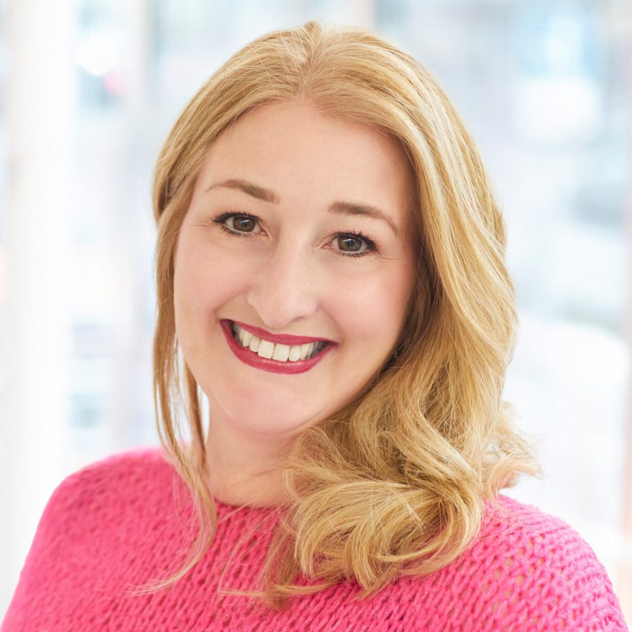 Ina Rottmüller Portrait Lächelnde Frau mit langen blonden Haaren, trägt ein pinkes Oberteil.