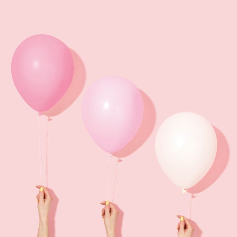 Coaching Prozess Drei Ballons in verschiedenen Rosatönen, gehalten von Händen vor einem pinken Hintergrund.