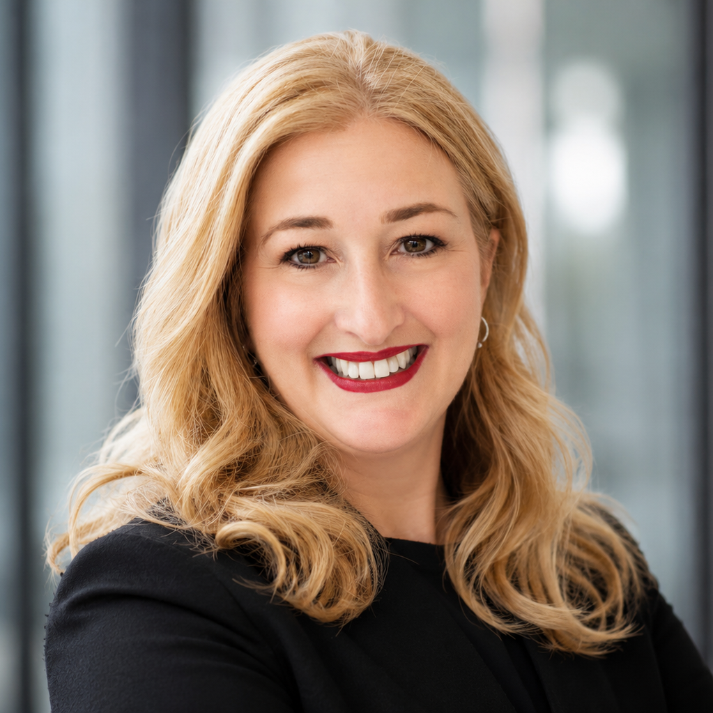 Lächelnde Frau mit blonden Haaren und schwarzer Bluse vor einem modernen Hintergrund.
